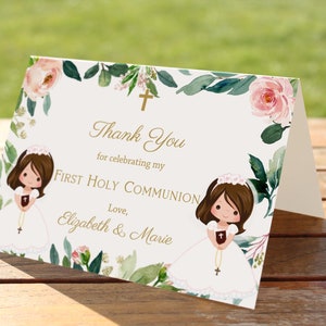 May include: Thank You for celebrating my First Holy Communion. Love, Elizabeth & Marie. White card with gold lettering and floral border. Two illustrations of girls in white dresses with rosaries.