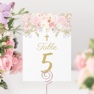May include: White table number card with a gold cross and the text "Table 5" in gold script. The card is decorated with a pink and white floral border.