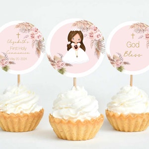 May include: Three pink and white cupcake toppers with a gold cross, floral design, and a girl in a white dress. The text on the toppers reads "Elizabeth's First Holy Communion May 20, 2024" and "God Bless".