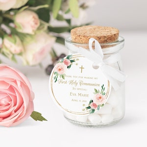 Pode incluir: Um pequeno frasco de vidro com tampa de corti&ccedil;a cheio de doces brancos. Uma fita branca est&aacute; amarrada ao redor do frasco com uma etiqueta redonda anexada. A etiqueta &eacute; branca com uma borda dourada e apresenta um design floral com flores rosa e folhas verdes. A etiqueta tamb&eacute;m inclui o texto "Obrigado por tornar a minha Primeira Comunh&atilde;o t&atilde;o especial! Eva Marie 15 de abril de 2019".