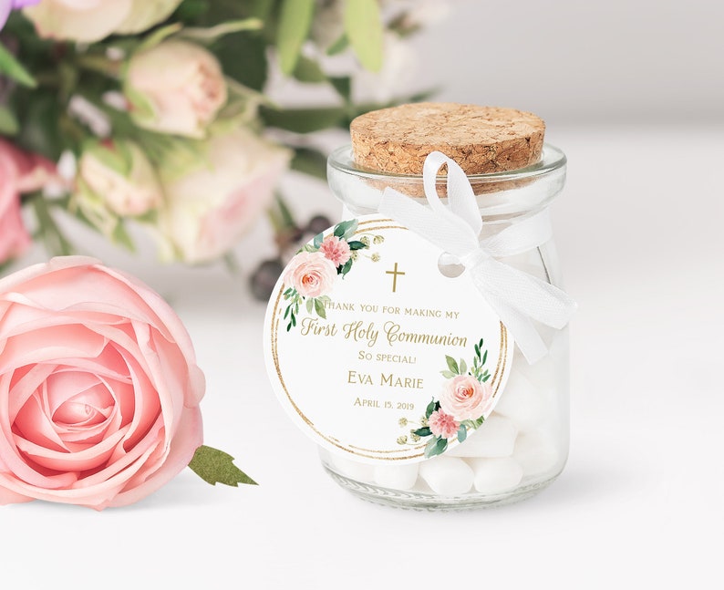 Pode incluir: Um pequeno frasco de vidro com tampa de corti&ccedil;a cheio de doces brancos. Uma fita branca est&aacute; amarrada ao redor do frasco com uma etiqueta redonda anexada. A etiqueta &eacute; branca com uma borda dourada e apresenta um design floral com flores rosa e folhas verdes. A etiqueta tamb&eacute;m inclui o texto "Obrigado por tornar a minha Primeira Comunh&atilde;o t&atilde;o especial! Eva Marie 15 de abril de 2019".