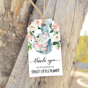 Op de afbeelding: Een wit bedankkaartje met een aquarel-illustratie van een grijze olifant met roze accenten, omringd door roze en witte bloemen. De tekst op het kaartje luidt "Bedankt voor het verwennen van onze lieve kleine pinda".