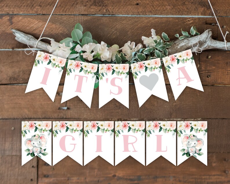 Op de afbeelding: Een baby shower banner met roze bloemen- en olifantendesigns. De banner luidt "It's a Girl" met een hart tussen de woorden "a" en "girl".