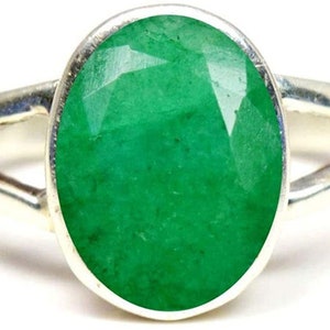 May include: A silver ring featuring a large, oval emerald gemstone. The ring has a simple, elegant design with a split band.