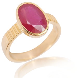 May include: A gold ring with a large, oval-shaped ruby gemstone. The ring has a textured band.