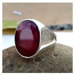 May include: A silver ring featuring a large, oval-shaped ruby gemstone. The ruby is a deep red colour and has a faceted cut.