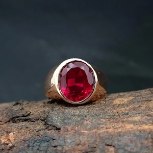 May include: A gold ring with a large, round, red gemstone.