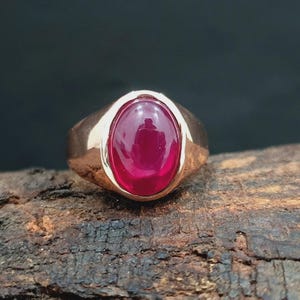 May include: A gold ring with a large, oval-shaped, red gemstone.