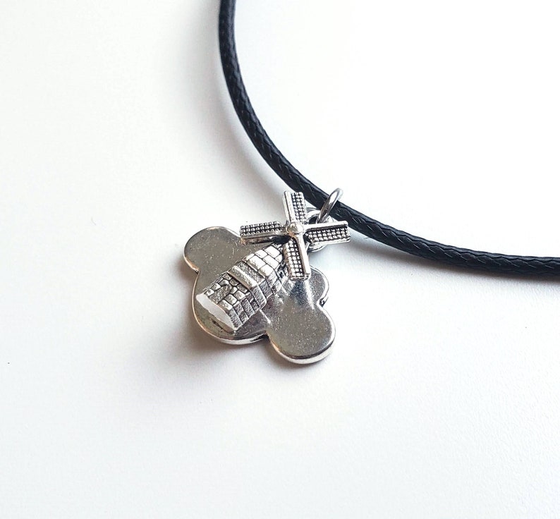 May include: A silver charm necklace with a black cord. The charm is a windmill on a cloud.