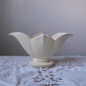 May include: A white ceramic flower-shaped vase with a wide opening and a rounded base.
