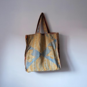 Könnte beinhalten: Eine große Tragetasche aus gewebtem Stoff mit einem blauen und gelben Muster. Die Tasche hat braune Lederriemen.