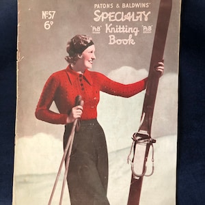 Könnte beinhalten: Ein Vintage-Strickbuchcover mit einer Frau in einem roten Pullover und einer schwarzen Hose, die Skistöcke hält und neben einem Paar Ski steht. Der Text auf dem Cover lautet "Patons & Baldwins' Specialty Knitting Book" mit dem "P&B" Markenzeichen.