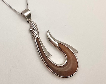 May include: A silver chain necklace with a brown and silver fish hook pendant. The hook is made of wood and silver and has a detailed design.