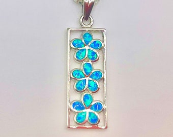 May include: A silver necklace with a pendant featuring three blue opal flowers in a rectangular frame.