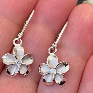 May include: A pair of silver flower earrings with a white enamel finish and a clear rhinestone in the center of each flower.