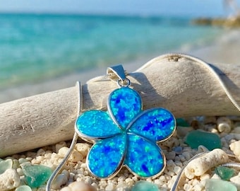 Könnte beinhalten: Eine silberfarbene Halskette mit einem fünfblättrigen Blumenanhänger, der mit schillerndem blauem und cyanfarbenem Material eingelegt ist. Der Anhänger ist an einer dünnen silberfarbenen Kette befestigt und zeigt eine lebendige, schimmernde Oberflächenstruktur.