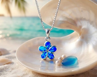 Può includere: Una collana a catena quadrata in argento con un ciondolo a forma di fiore a cinque petali con un inserto iridescente blu brillante. Il ciondolo poggia all'interno di una grande conchiglia color crema liscia con tre piccole perle e un vetro blu.