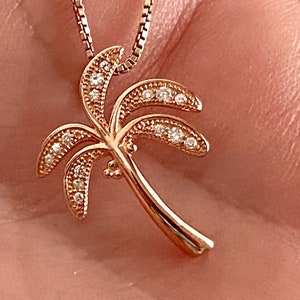 May include: A rose gold palm tree pendant necklace with clear cubic zirconia stones.