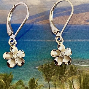 May include: Silver dangle earrings with a small white flower charm. The flower has a small clear stone in the center.