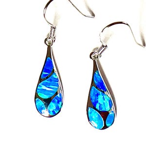 May include: A pair of silver teardrop earrings with a vibrant blue and white opal-like inlay. The earrings have a hook closure and a polished finish, showcasing a modern and elegant design.