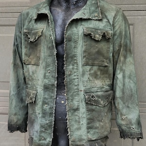 May include: A distressed green jacket with multiple pockets and a button-up front. The jacket has a worn appearance with frayed edges and visible wear and tear, suggesting a vintage or rugged aesthetic. The jacket is displayed on a mannequin.