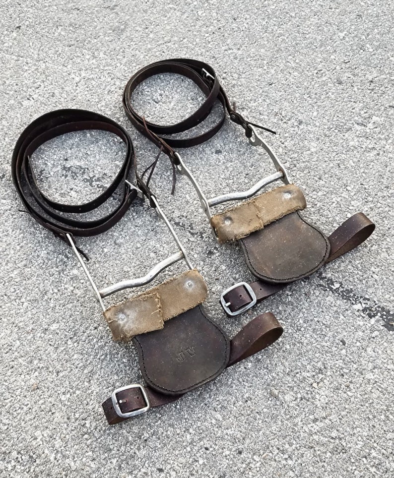 May include: Two pairs of brown leather stirrups with silver metal buckles and straps. The stirrups have a worn, distressed look and are marked with the initials "JV".