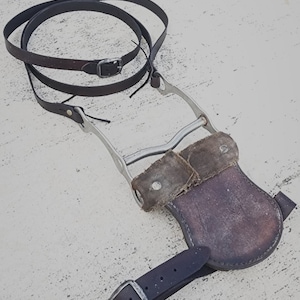 May include: A brown leather strap with a silver metal stirrup and a brown leather flap. The strap is wrapped around the stirrup and the flap is attached to the stirrup.