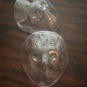 Puede incluir: Dos máscaras de Halloween de plástico transparente. La máscara superior es de forma ovalada simple. La máscara inferior es una máscara de hockey más detallada con agujeros y aberturas para los ojos.