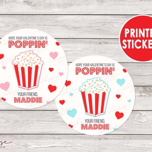 Puede incluir: Dos pegatinas redondas para el D&iacute;a de San Valent&iacute;n con un cubo de palomitas de ma&iacute;z y corazones. El texto en las pegatinas dice "Espero que tu D&iacute;a de San Valent&iacute;n sea Poppin'" y "Tu amigo, Maddie".