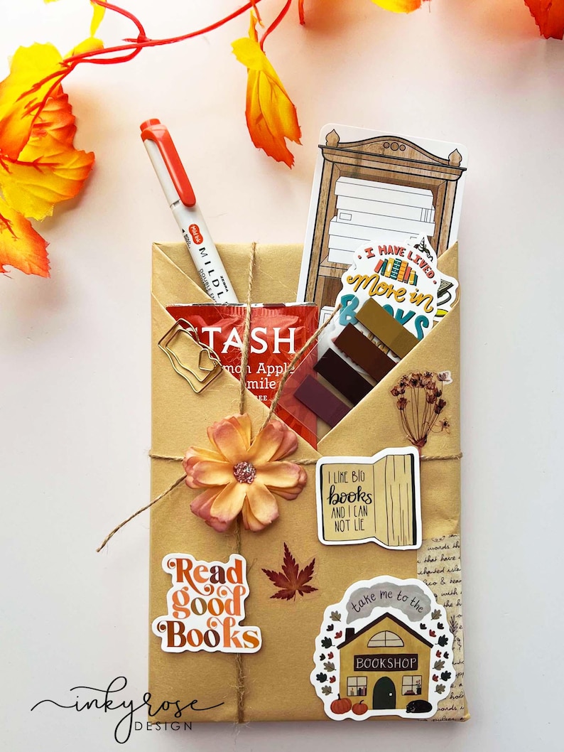 A fall-themed Blind Date with a Book bundle wrapped in kraft paper and twine, decorated with autumn stickers like a pumpkin and books, and includes a highlighter, tea, book tabs, and a bookmark, adorned with a flower, giving off cozy fall vibes.