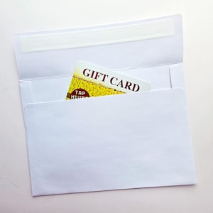 May include: A white paper envelope with an open flap containing a rectangular gift card. The card features a yellow beer-themed graphic with bubbles and the text GIFT CARD and TAP HOUSE printed in dark red letters on the front surface.