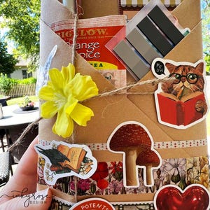 A fall-themed Blind Date with a Book bundle wrapped in kraft paper and twine, decorated with autumn stickers and includes a highlighter, tea, book tabs, and a bookmark, adorned with a flower, giving off cozy fall vibes.