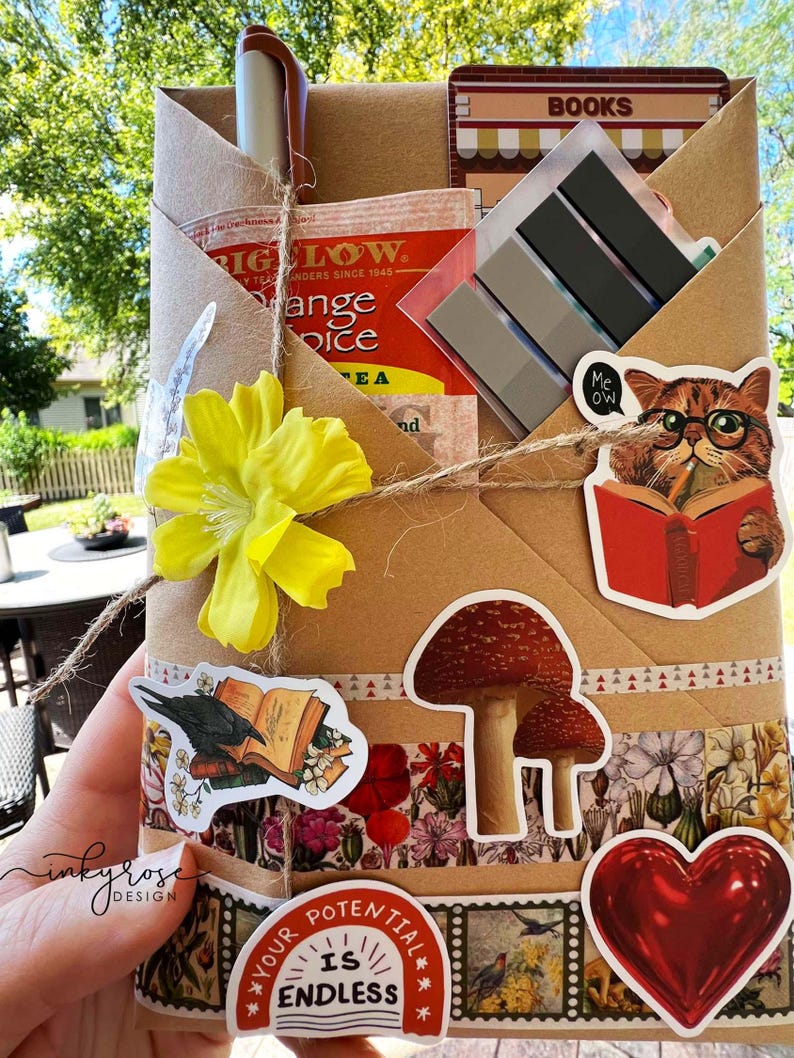 A fall-themed Blind Date with a Book bundle wrapped in kraft paper and twine, decorated with autumn stickers and includes a highlighter, tea, book tabs, and a bookmark, adorned with a flower, giving off cozy fall vibes.