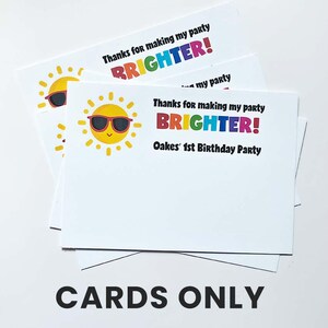 K&ouml;nnte beinhalten: Ein Stapel wei&szlig;er rechteckiger Dankeskarten mit einer gelben Sonnengrafik, die eine schwarze Sonnenbrille tr&auml;gt. Der Text lautet: Thanks for making my party BRIGHTER! Oakes' 1st Birthday Party. Unten steht in schwarzer Schrift CARDS ONLY.