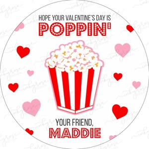Puede incluir: Un c&iacute;rculo blanco con corazones rojos y rosas y el texto "HOPE YOUR VALENTINE'S DAY IS POPPIN'" en rojo con lunares blancos. Un cubo de palomitas de ma&iacute;z a rayas rojas y blancas con palomitas de ma&iacute;z blancas est&aacute; en el centro. El texto "YOUR FRIEND, MADDIE" est&aacute; en rojo con lunares blancos en la parte inferior.