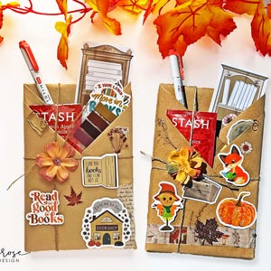 May include: Two brown paper packages wrapped with twine and decorated with fall-themed stickers, including a fox, a scarecrow, a pumpkin, and a bookshelf. The packages also include tea bags, a pen, and a book-themed sticker that says "Read good books".