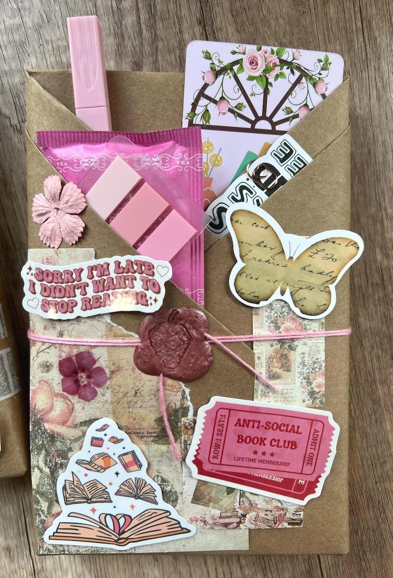 May include: A brown paper package tied with pink string, adorned with stickers, a pink clip, and a wax seal. Stickers include a butterfly, open books, and text that reads "Sorry I'm late I didn't want to stop reading." Also includes an "Anti-Social Book Club" ticket.