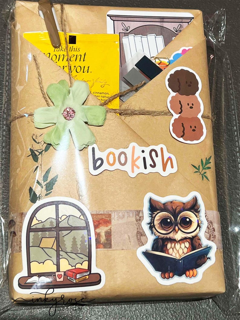 A fall-themed Blind Date with a Book bundle wrapped in kraft paper and twine, decorated with autumn stickers like an owl  and books, and includes a highlighter, tea, book tabs, and a bookmark, adorned with a flower, giving off cozy fall vibes.