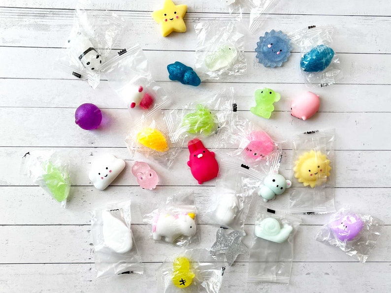 May include: Assortment of colorful, small, squishy toys in various shapes, including a cloud, a star, a sun, a snail, a unicorn, a chick, a flower, a heart, a frog, a fish, a ladybug, a panda, a ghost, and a ball. The toys are packaged in clear plastic bags.