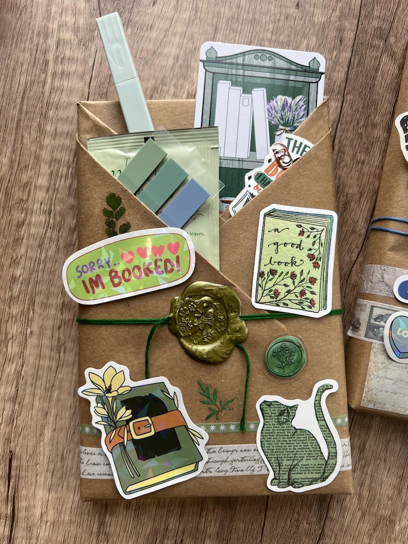 May include: A wrapped package with stickers and a wax seal. The package is brown with green twine and features stickers with book and cat illustrations, and the text "SORRY... IM BOOKED!". A light green highlighter and sticky notes are visible.