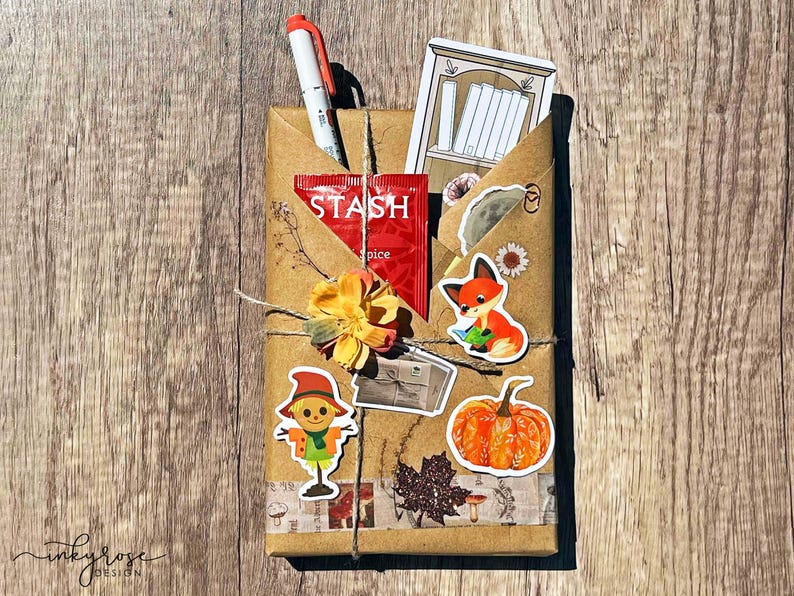 A fall-themed Blind Date with a Book bundle wrapped in kraft paper and twine, decorated with autumn stickers like a scarecrow and pumpkin, and includes a highlighter, tea, book tabs, and a bookmark, adorned with a flower, giving off cozy fall vibes.