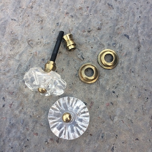 Puede incluir: Un juego de cuatro pomos de puerta de cristal transparente con acabado dorado. Los pomos son de diferentes formas y tamaños, incluyendo un pomo redondo, un pomo cuadrado y un pomo con diseño floral.