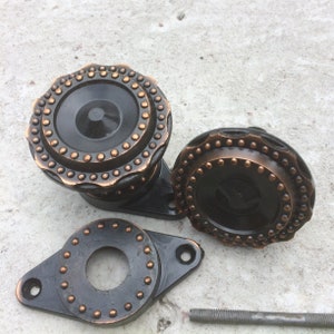 Puede incluir: Tres pomos de metal negro con acabado de cobre y un patrón decorativo de pequeños puntos. Los pomos son redondos y tienen un agujero en el centro.