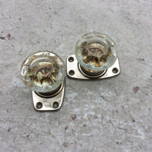 Op de afbeelding: Twee antieke glazen deurknoppen met sierlijke ontwerpen, gemonteerd op zilveren platen.