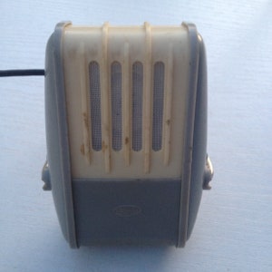 May include: A vintage gray and white microphone with a metal grill and the word "Grundig" printed on the bottom.