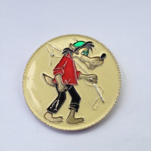 May include: A yellow and white enamel pin featuring a cartoon wolf wearing a green hat and holding a fishing rod. The wolf is walking to the right and has a red shirt and black pants.