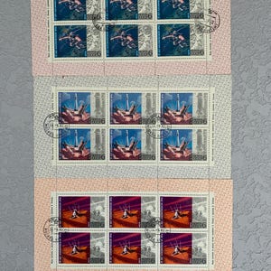 Könnte beinhalten: Drei Blätter mit sowjetischen Briefmarken aus der Zeit der Sowjetunion mit Bildern von Kosmonauten in Raumanzügen, einem Raketenstart und einem Weltraumspaziergang. Die Briefmarken sind in neuwertigem Zustand und wurden nie verwendet.