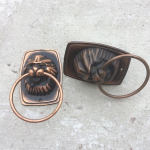 Puede incluir: Dos anillos para toallas de estilo antiguo con diseños de cabeza de león. Los anillos son de metal y tienen un acabado marrón oscuro.