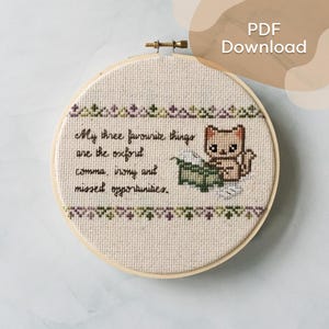 May include: A cross-stitch embroidery hoop with the text "My three favourite things are the oxford comma, irony and missed opportunities." A cartoon cat is next to the text. The top and bottom of the design have a decorative border.