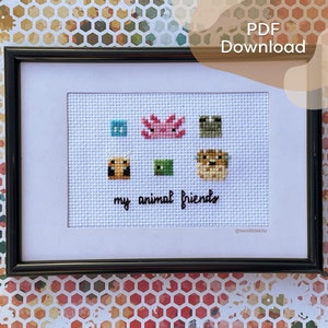 Puede incluir: Arte en punto de cruz enmarcado con diseños de animales pixelados de colores. La obra de arte incluye un cuadrado azul, un ajolote rosa, un cuadrado verde, un cuadrado marrón, un cuadrado verde y un animal beige. El texto "my animal friends" está bordado debajo. El marco es negro.